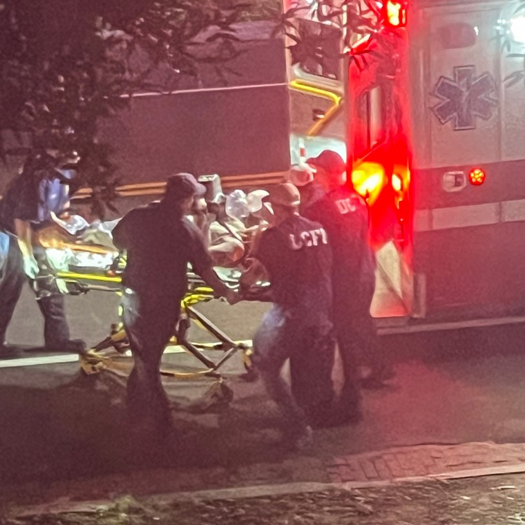 A person is wheeled from his home into an ambulance outside, EMTs surround him